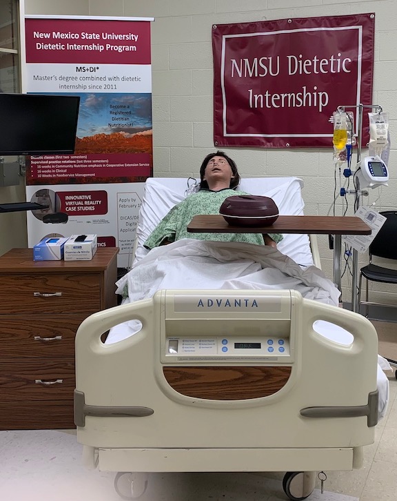 Image of the NMSU dietetic internship simulation lab that includes: mannequin, hospital bed, hospital table and computer monitor